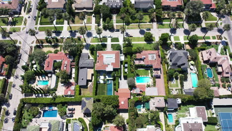 Drone-shot-flying-over-beautiful-West-Hollywood,-Los-Angeles,-California-neighborhood-filled-with-palm-tree-lined-streets,-cars-driving-and-parked,-mansions-and-swimming-pools