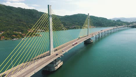 Cinematic-aerial-shot-bridge-traffic-above-the-turquoise-color-ocean,-located-in-Laguna,-Santa-Catarina,-Brazil