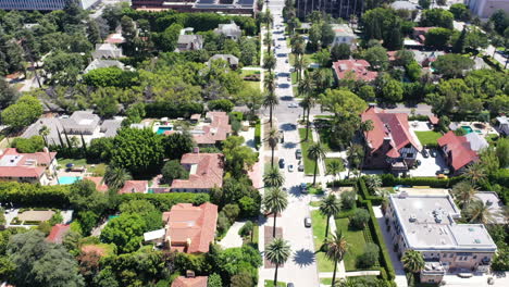 Drone-follows-white-car-driving-up-palm-tree,-house-lined-street,-in-beautiful-West-Hollywood,-California