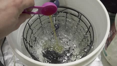 Pouring-a-scoop-of-chemicals-in-water-for-plant-food--slow-motion