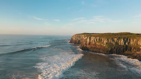Drone-aerial-view-of-tropical-beach-rocky-cliffs-on-atlantic-ocean-at-sunrise