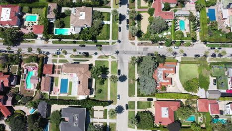 Drone-zooms-out-to-reveal-palm-tree-lined-streets-with-cars-driving,-and-mansions-in-West-Hollywood,-California