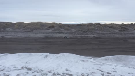Man-on-quad-bike-traveling-on-black-sandy-beach-in-coastal-Iceland,-aerial