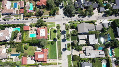 Drone-flying-over-palm-tree-lined-streets-with-mansions-and-sun-glistening-swimming-pools-in-West-Hollywood,-Los-Angeles,-California