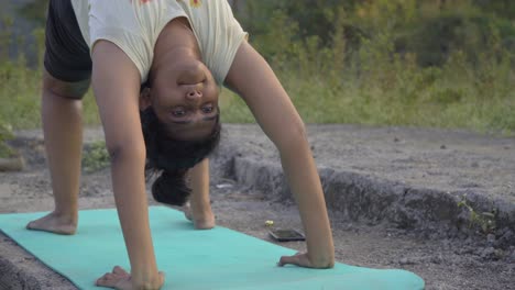 Indian-girl-doing-upward-bow-weel-pose-urdhva-dhanurasana-yoga-pose-by-the-lakeside-face-close-front-shot