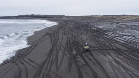 Aerial-of-quad-bike-riding-on-black-sand-beach-in-volcanic-Iceland