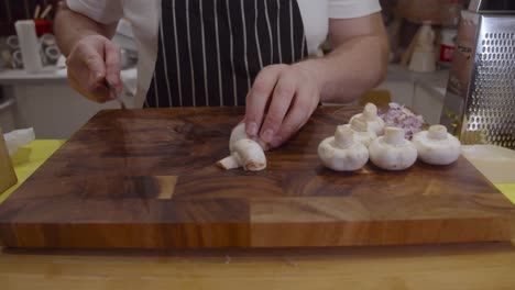 Chef-cuts-white-mushrooms-on-wooden-cut-board-in-the-kitchen