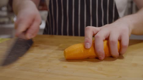 Chef-cuts-carrot-into-pieces-on-wooden-cut-board
