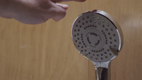 Hand-taps-clogged-shower-head-as-water-trickles