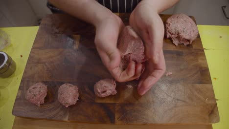 Close-up-on-chef-hands-forming-meat-balls-and-lay-them-on-top-of-wooden-cut-board