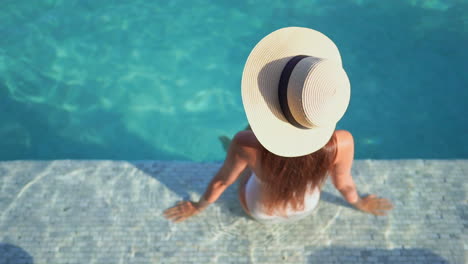 Woman-In-Swimsuit-and-Summer-Hat-Sitting-on-a-Pool-Edge,-High-Angle-View