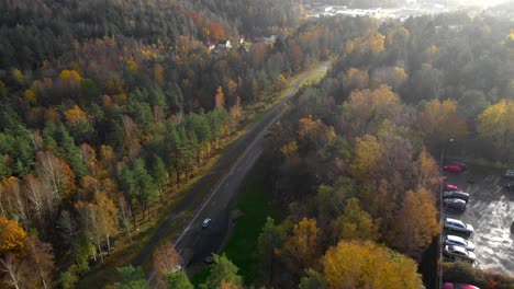 Aerial-view-of-cars-passing-on-a-forest-road-in-autumn-with-beautiful-autumnal-colored-trees,-travel-concept