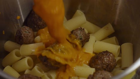 Adding-vegetable-sauce-to-pasta-with-meat-balls,-inside-metal-cooking-pot
