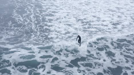 Surfer-riding-whitewash-wave-with-low-speed-in-Iceland,-aerial
