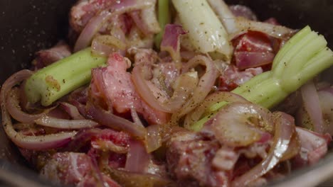 Stirring-beef-shank-mixed-with-onion-slices,-celery-and-spices-with-wooden-spoon-inside-deep-cooking-pot