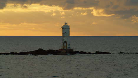 Solitary-lighthouse-on-tiny-isle-against-sunlit-horizon-at-golden-hour