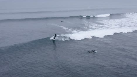 Surfers-having-fun-in-super-cold-water-of-Atlantic-Ocean-in-Iceland,-aerial