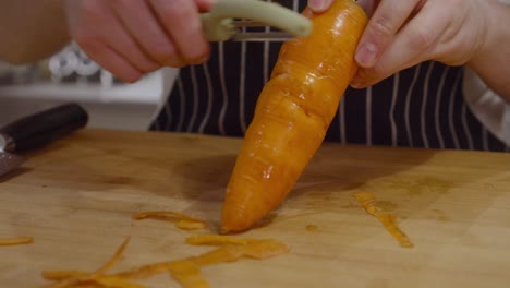 Koch-Schält-Karottenhaut-Mit-Einem-Schälmesser-Auf-Holzschnittbrett
