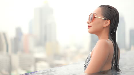 Junge-Stilvolle-Asiatische-Frau-Im-überlaufpool-Auf-Dem-Dach-Mit-Atemberaubendem-Blick-Auf-Die-Stadt