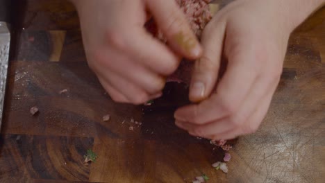 Close-up-on-hands-mashing-meat-on-wooden-cut-board-fro-making-meatballs