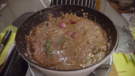 Adding-water-into-a-deep-cooking-pot-with-beef-shank,-onion-slices,-celery-and-spices-cooked-inside