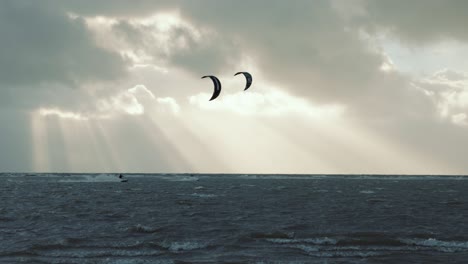 Kitesurfers-Triturando-En-Tormenta,-Mientras-El-Sol-Brilla-A-Través-De-Nubes-Oscuras