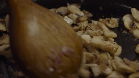 Stirring-and-mixing-up-white-mushrooms-with-onion-slices-inside-hot-frying-pan