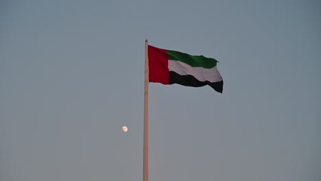 Bandera-De-Los-Emiratos-árabes-Unidos-Ondeando-En-El-Aire-Primer-Cuarto-De-Luna-En-El-Fondo,-El-Símbolo-Nacional-De-Los-Emiratos-árabes-Unidos,-Día-Nacional-De-Los-Emiratos-árabes-Unidos-2020,-Video-4k