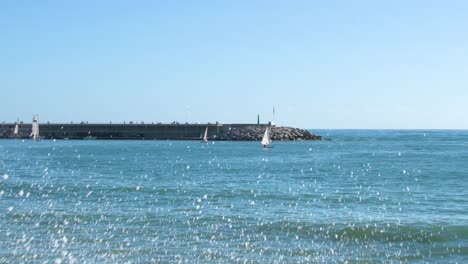 Sailing-boats-sailing-near-the-harbor-and-people-strolling-away-on-the-jetty