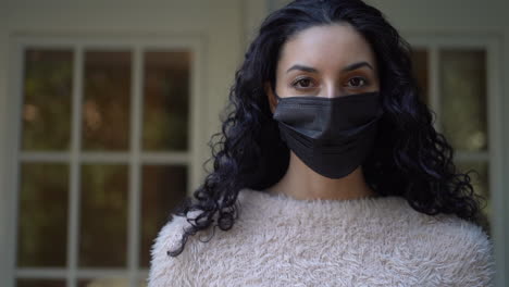 Beautiful-young-Latina-woman-wearing-a-black-face-mask-and-looking-directly-at-the-camera