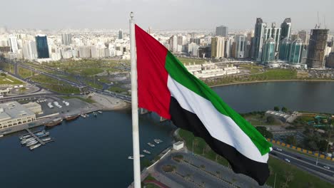 Top-closeup-view-of-the-Flag-of-the-United-Arab-Emirates-waving-in-the-air-over-Sharjah's-Flag-Island,-The-national-symbol-of-United-Arab-Emirates,-UAE-National-Day,-4K-Video