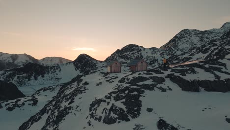 Person-is-standing-behind-two-wooden-huts-at-sunrise-in-the-Austrian-alps
