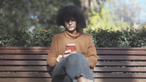 Introvert-curly-girl-texting-alone-on-a-bench-at-a-park