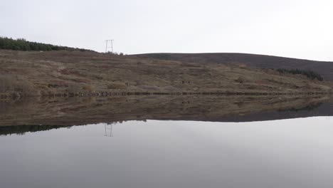 Mirror-like-lake-Vifilsstadavatn,-flat-water-surface-reflecting-hills-and-sky