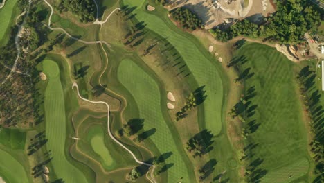 Aerial-overhead-shot-of-a-golf-course-with-beautiful-abstract-patterns,-sand-traps,-trees-and-lakes