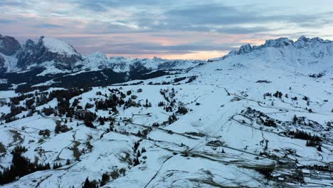 Panoramic-aerial-shot-of-snowy-alpine-meadow-Seiser-Alm---Alpe-di-Siusi-plateau-and-Dolomite-mountain-range-in-South-Tyrol,-Italy-at-sunset