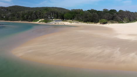 Rotating-drone-shot-of-the-Korogoro-Creek-with-wind-blowing-sand-across-a-sand-bar-at-Hat-Head-New-South-Wales,-Australia