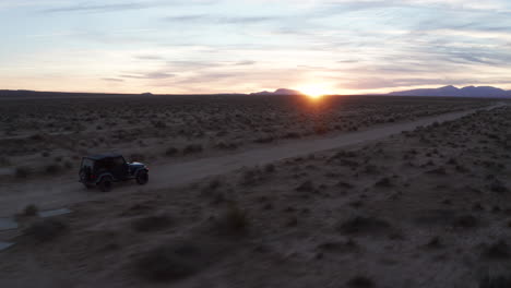 Jeep-going-down-a-dirt-trail-in-the-Mojave-Desert-at-sunset---aerial-follow