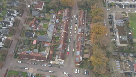 High-aerial-of-white-car-driving-over-small-street-in-beautiful-suburban-neighbourhood
