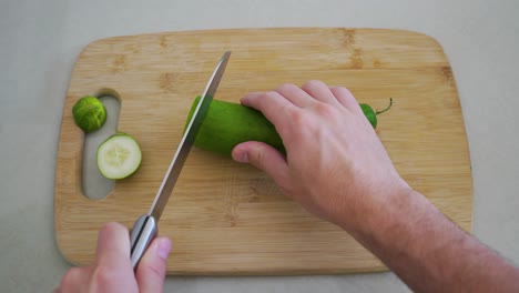 First-Person-POV-View-of-Man-Slicing-Cucumber-on-Wooden-Cutting-Board-with-Knife
