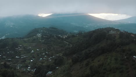Drone-aerial-flying-over-a-beautiful-green-valley-during-a-cloudy-sunset,-god-rays,-volcanic-landscape-in-Guatemala