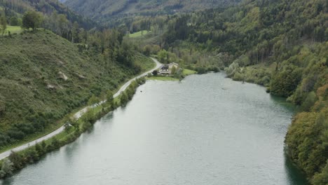 South-shore-of-Freibach-reservoir-dam-in-Austria-with-Stauseewirt-Greek-eatery-lodge-at-the-far-side,-Aerial-approach-tilt-up-view
