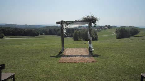 outdoor-wedding-setting-with-chairs,-arch-and-carpet-on-field,-wide-dolly-forward