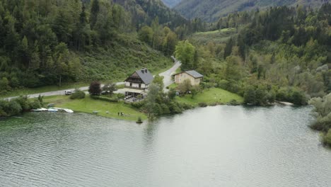 South-shore-of-Freibach-reservoir-dam-in-Austria-with-Stauseewirt-Greek-restaurant-and-cottage-with-people-left,-Aerial-orbit-advancing-view