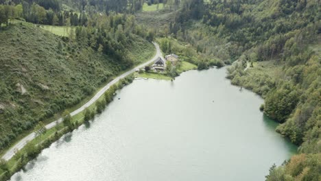 Freibach-reservoir-dam-South-shore-in-Austria-with-Stauseewirt-Greek-restaurant-lodge-below,-Aerial-approach-rotation-shot