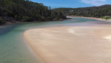 Cinematic-drone-shot-of-the-Korogoro-Creek-with-wind-blowing-sand-across-a-sand-bar-at-Hat-Head-New-South-Wales,-Australia