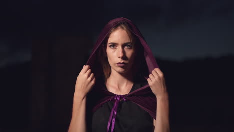 Mysterious-woman-wearing-a-purple-cape-slowly-putting-the-hood-over-her-head-and-staring-at-the-camera
