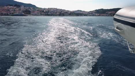 Slow-motion-shot-of-a-trail-and-foamy-waves-on-blue-sea-surface-behind-of-moving-boat-moving-away-from-land