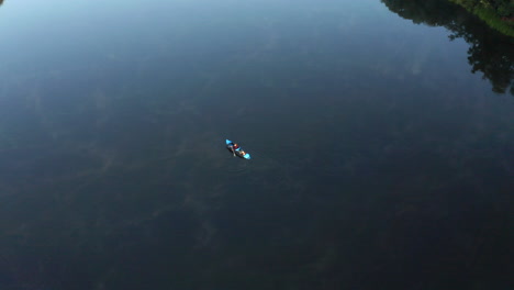 Drone-aerial-footage-of-topdown-kayak-with-people-slowly-paddling-on-a-calm,-relaxing-lake-with-stunning-reflection