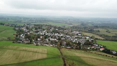 Small-village-surrounded-by-green-countryside-and-farmland,-Aerial-flyover-Carrmunock,-Glasgow